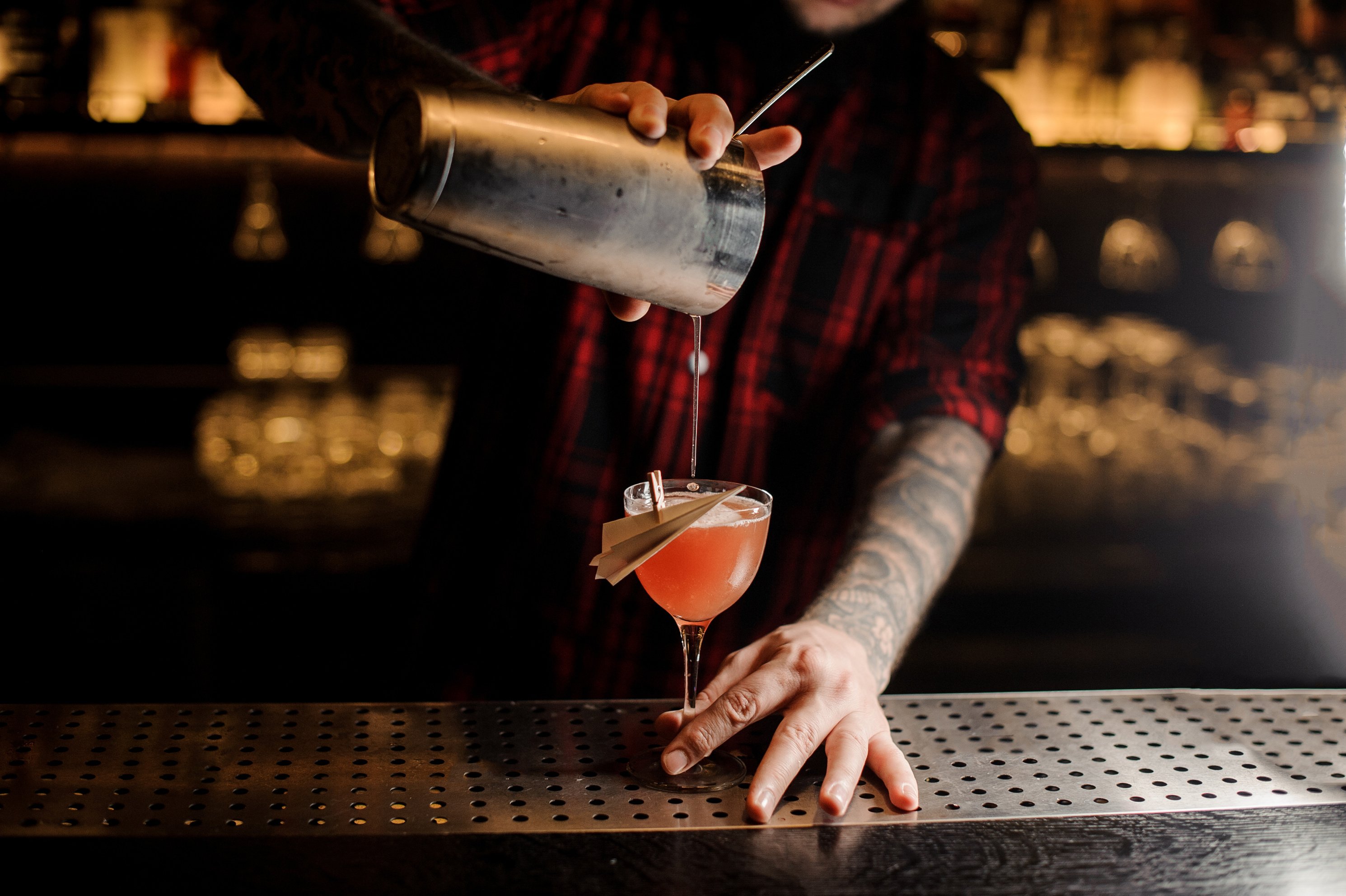 Barman pouring fresh Paper Plane cocktail into a decorated glass